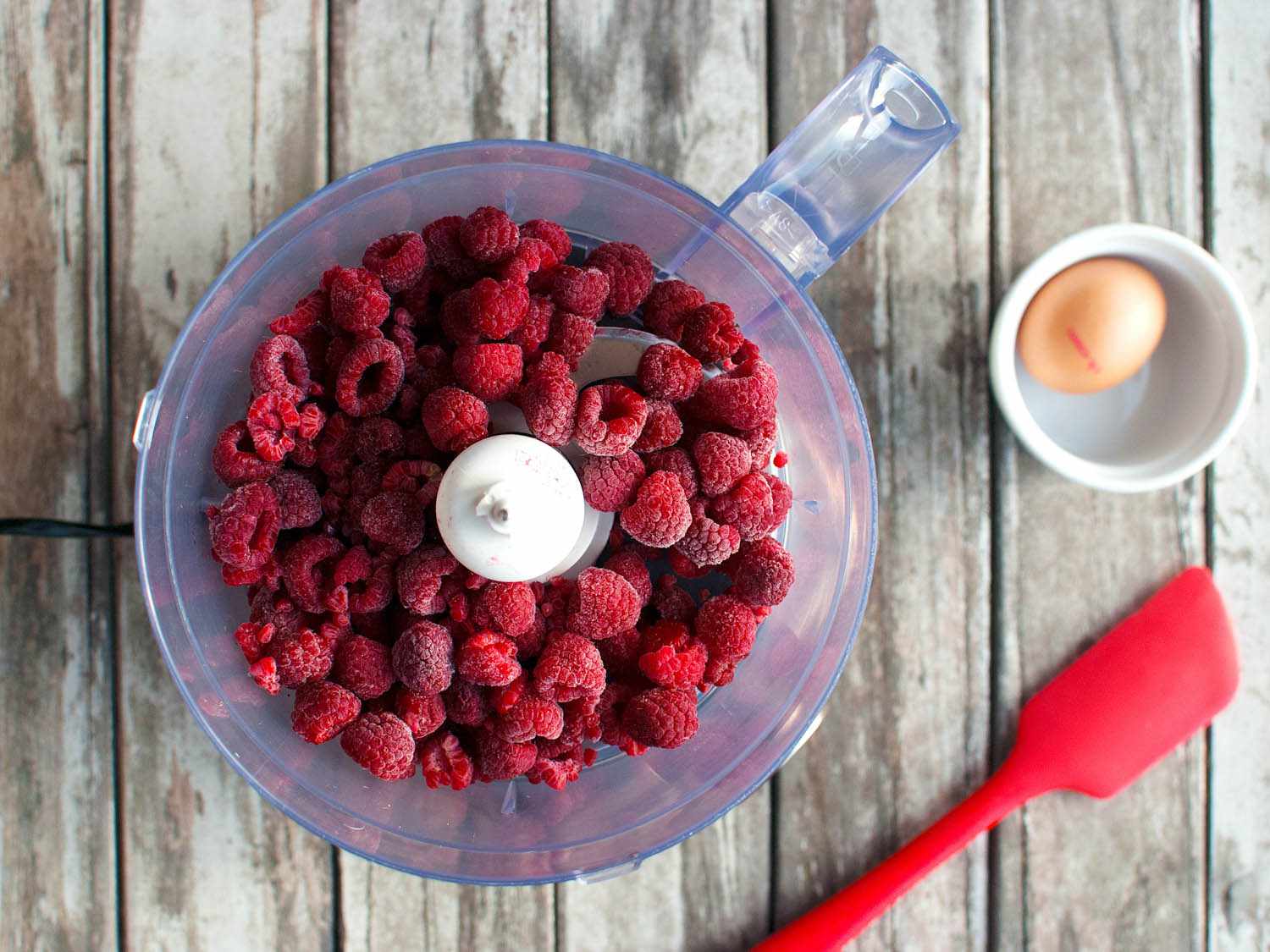 A food processor filled with frozen raspberries ready to be pureed into fruit mousse