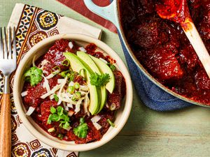 Overhead view of a bowl of chili con carne topped with avocado slices and cilantro next to the pot of chili. 