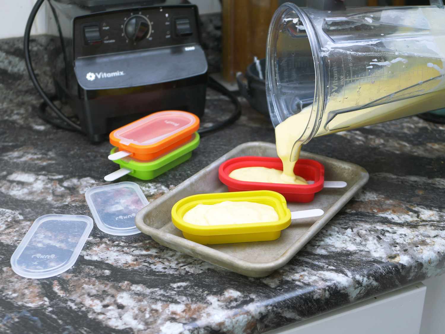 pouring popsicle filling mixture from a blender into molds on a countertop