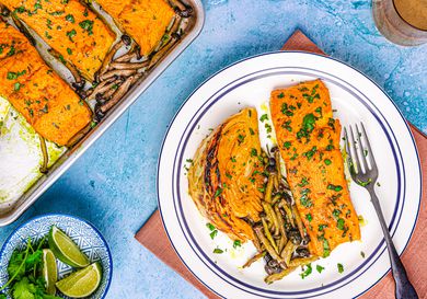 A plated salmon dish alongside a sheet pan with prepared salmon and vegetables, garnished and ready to serve