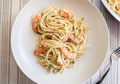A plate with spaghetti and shrimp, garnished with herbs, placed on a table with a fork nearby