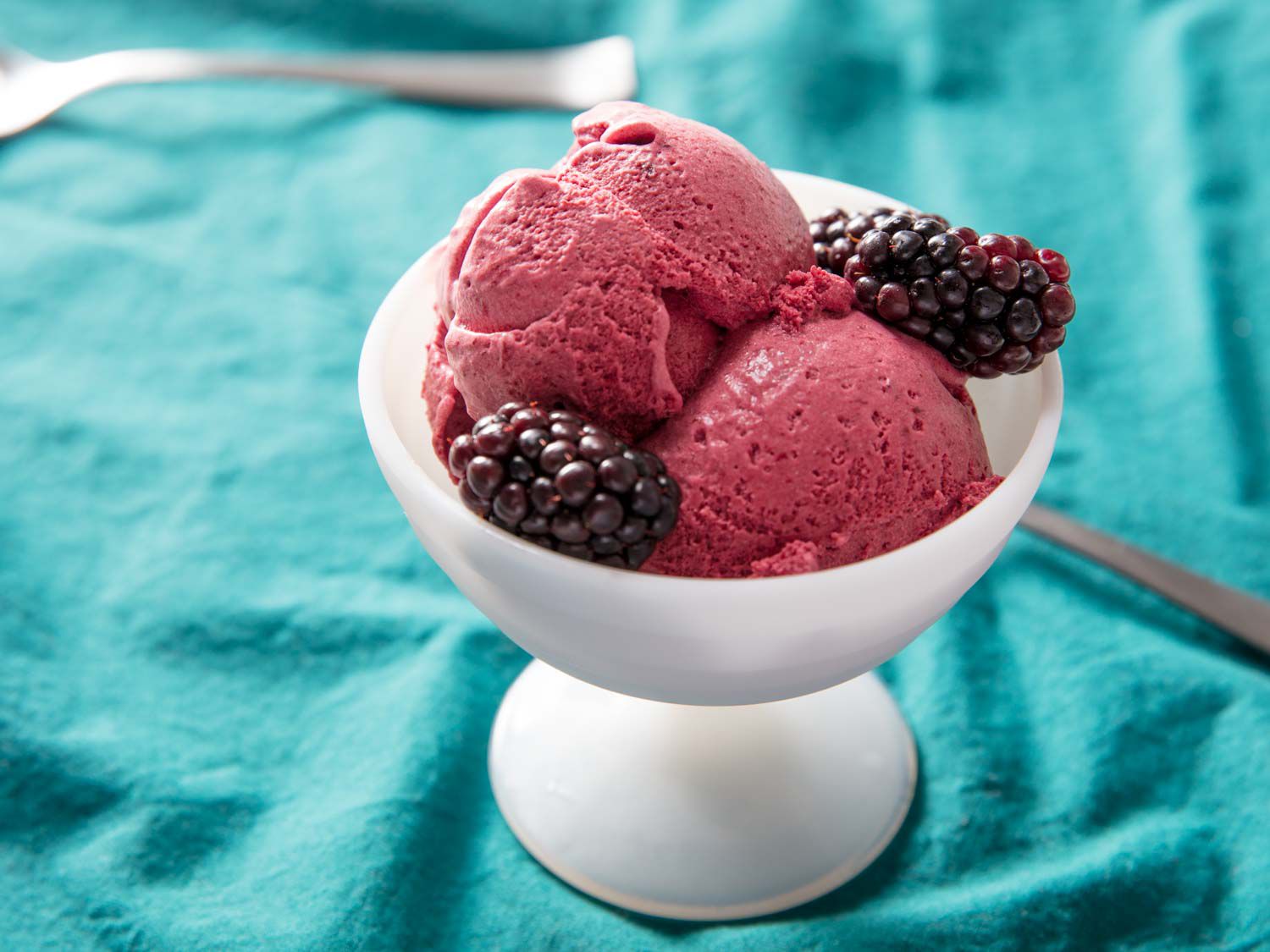 Closeup of two scoops of blackberry ice cream in a white parfait glass, garnished with a few fresh blackberries.