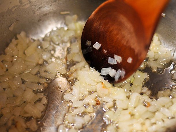 Diced onions being sauteed in oil in a saucepan and stirred with a wooden spoon.