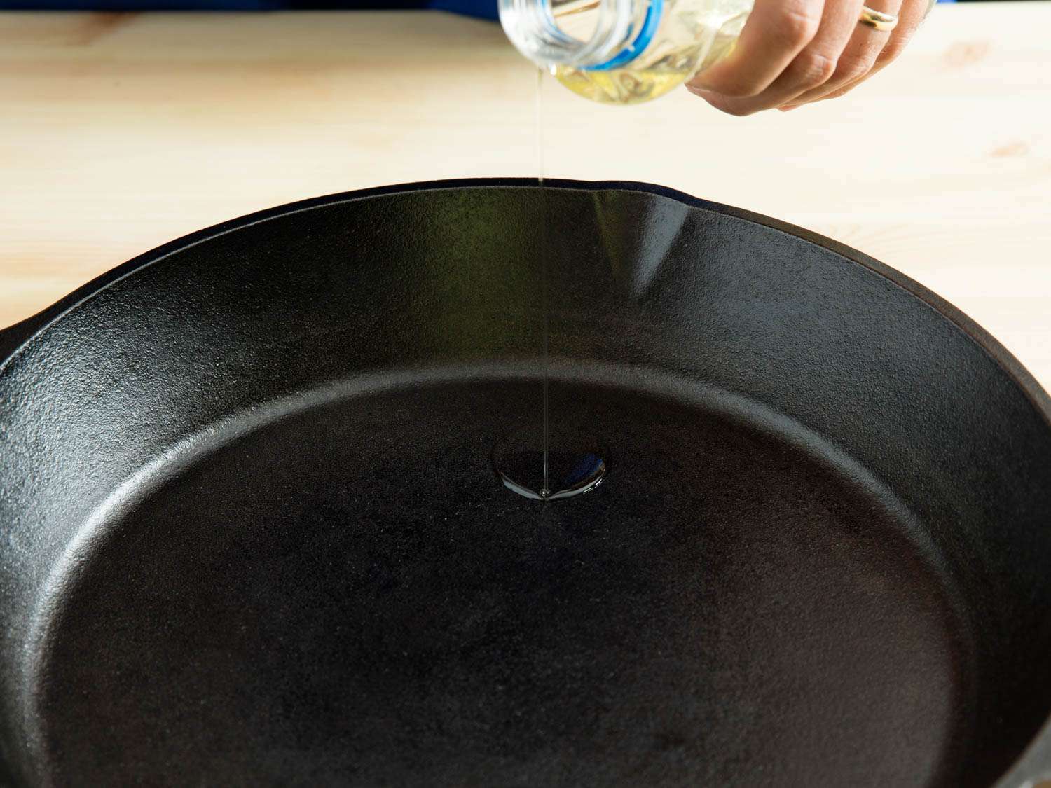 Drizzling fresh oil into a cleaned and dried cast iron pan in order to season it.