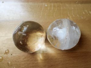 A clear sphere of ice to the left of a cloudy sphere of ice. 