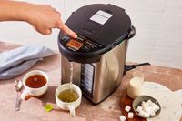 A person using the Zojirushi hot water dispenser to dispense hot water into a cup.
