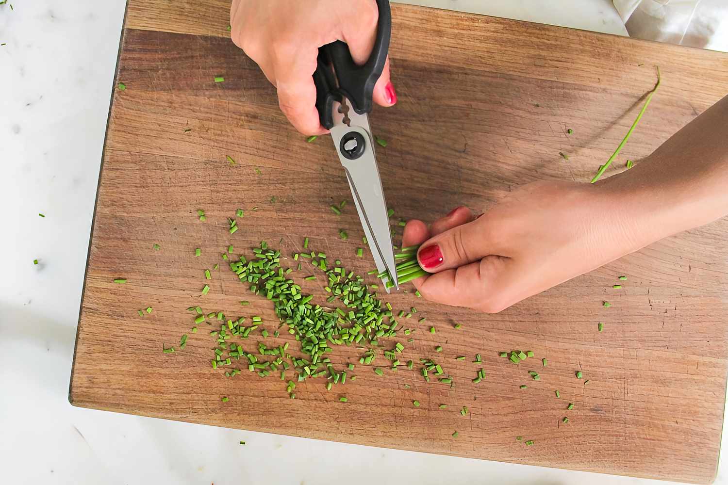Herb scissors cutting chives on a wooden cutting board