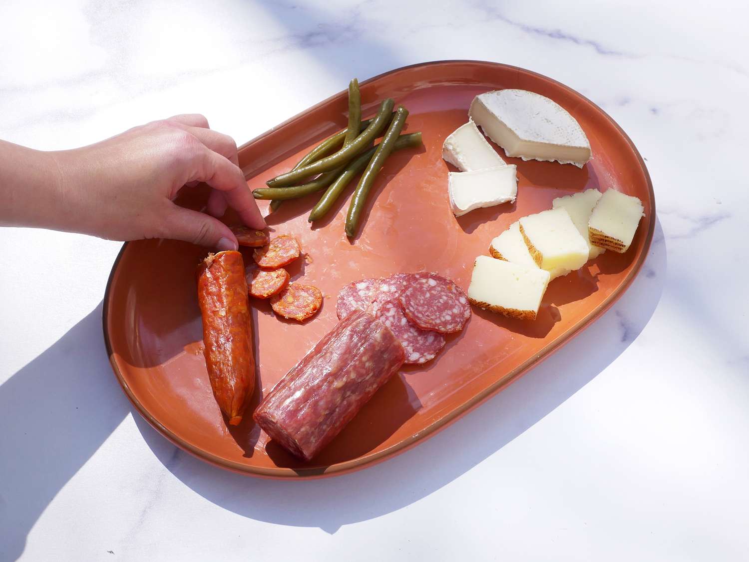 a hand taking a piece of salami from the our place serving platter