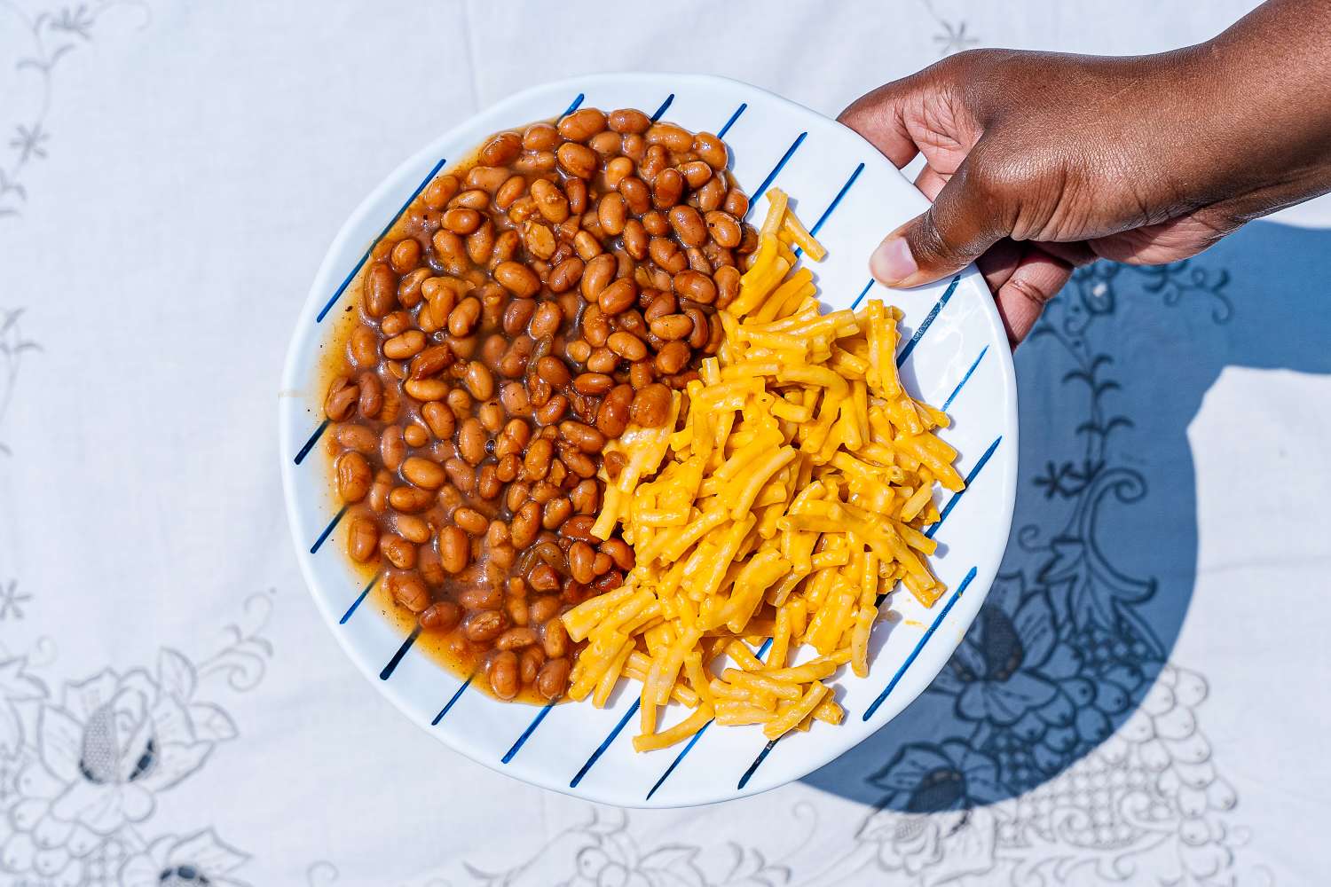 A hand holding a Lenox Blue Bay Melamine Dinnerware Set plate with baked beans and macaroni and cheese