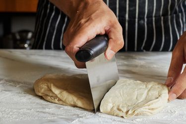 A person uses a bench scraper to cut a large piece of dough