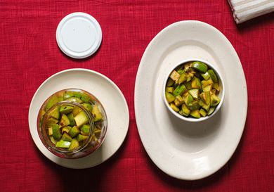 Mango pickle in a glass jar, and in a ramekin on a plate, on top of a red tablecloth