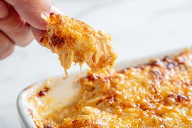 A closeup of a hand holding a scoop of baked dip with melted cheese from a dish