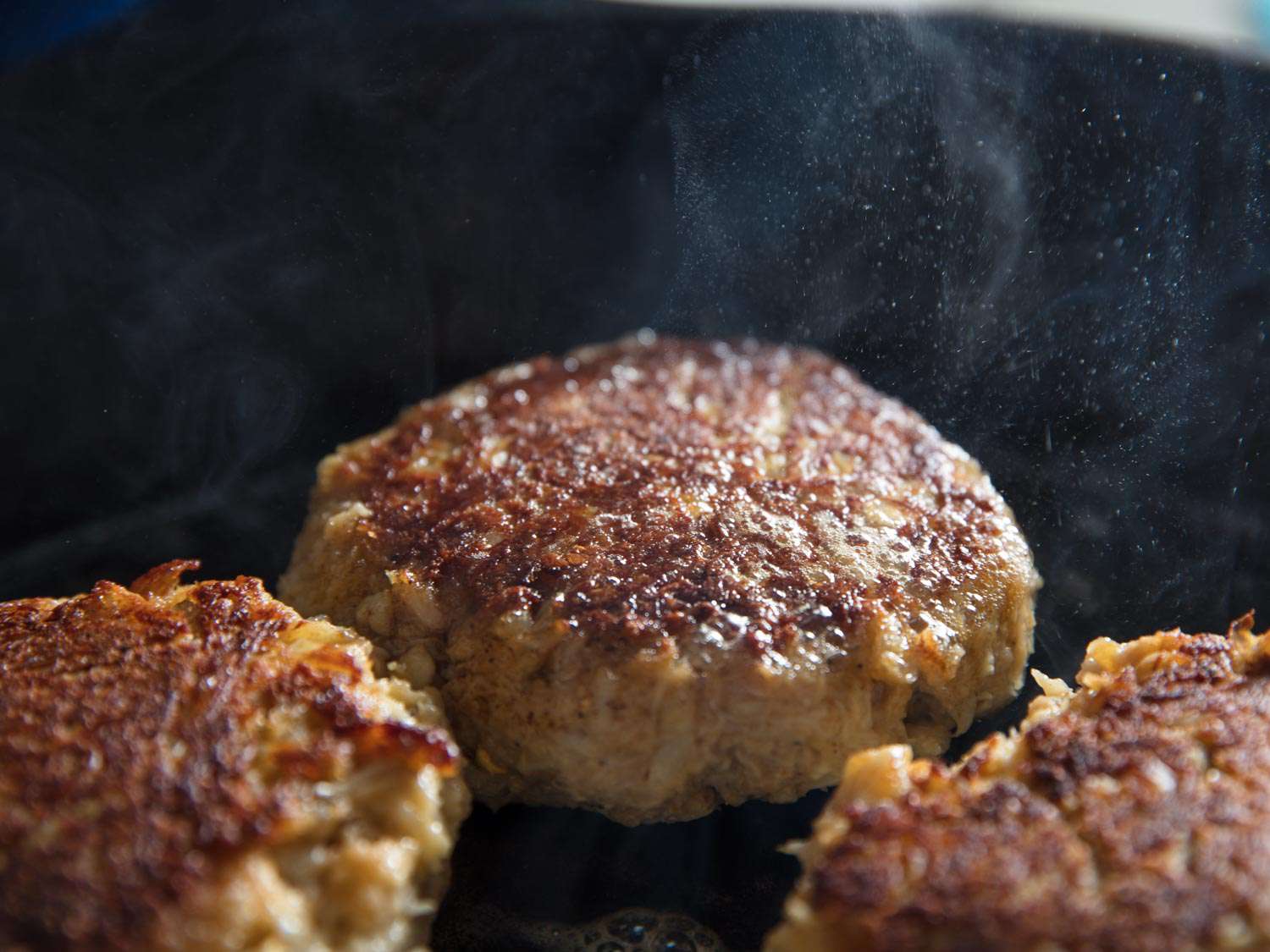 Closeup of Maryland crab cakes cooking in a cast iron skillet.