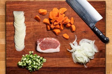 Overhead view of a cutting board showcasing multiple types of cuts of carrots, radishes, onions, meat, and cucumbers
