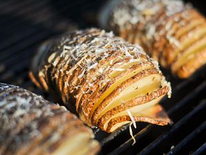 Closeup of Grilled Hasselback Potatoes With Garlic and Parmesan cooking on a grill grate.