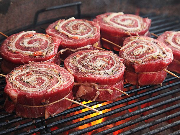 Stuffed and rolled flank steaks on barbecue with flames below