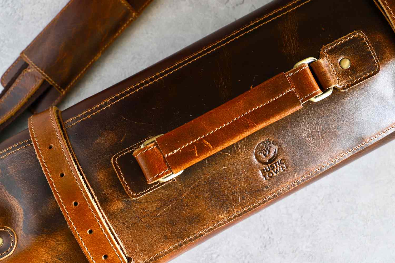 A detailed view of a Rustic Town Genuine Leather Chef Knife Roll with straps and a logo
