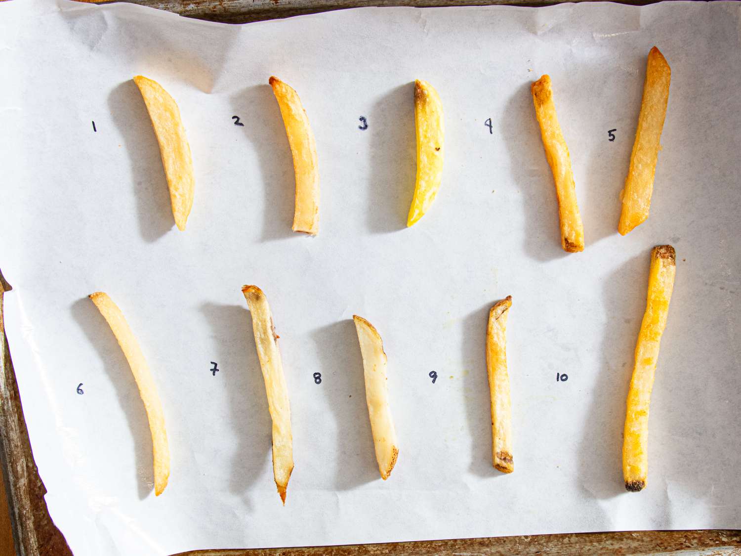Ten numbered French fries arranged on a sheet of parchment paper for a taste test