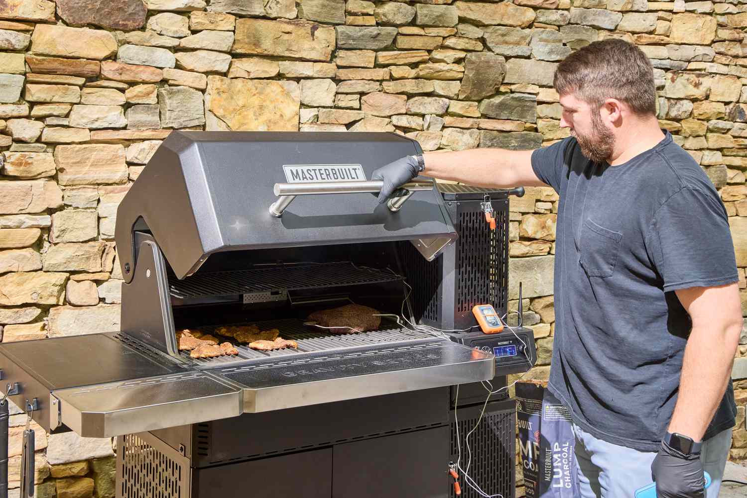 A person opens the door on the Masterbuilt Gravity Series 1150 Digital Charcoal Grill and Smoker