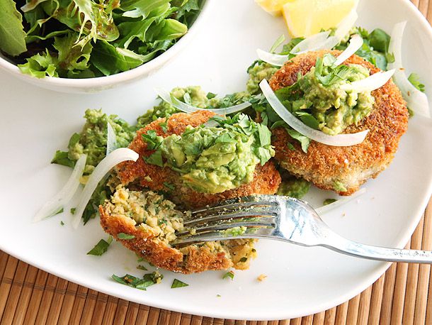 Avocado-topped crispy chickpea patties on a white plate, with one patty being broken into with a fork.