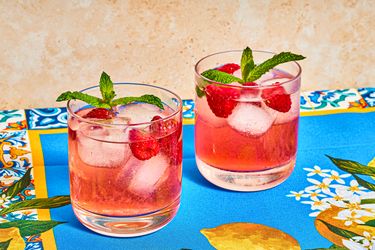 Two glasses of raspberry spritz garnished with mint leaves, placed on a colorful patterned surface