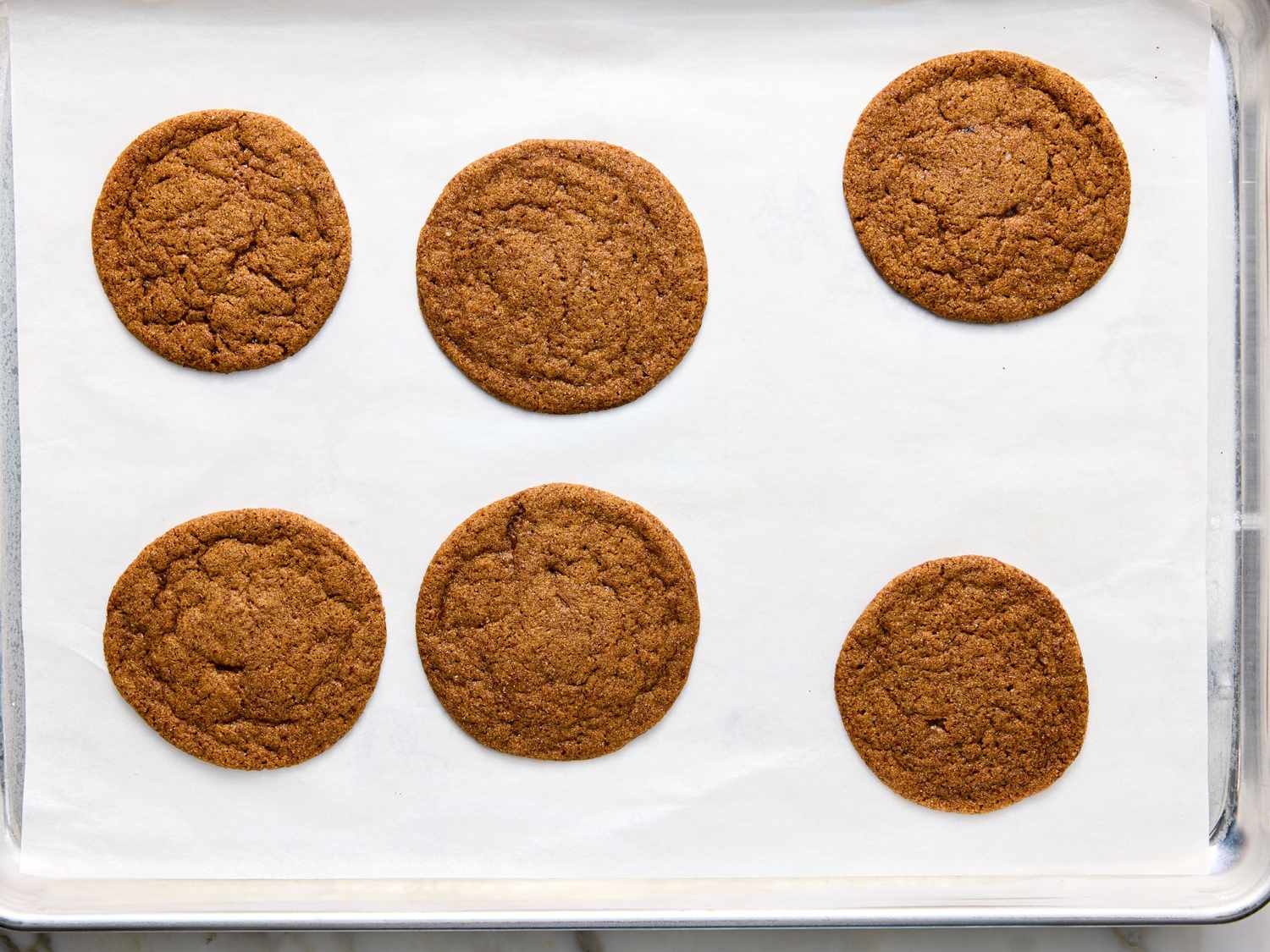 Six round cookies on a parchmentlined baking sheet evenly spaced in two rows appearing baked and ready