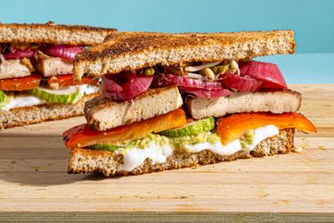 A marinated tofu sandwich layered with vegetables and spread on whole grain bread