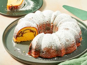 A bundt cake with a slice removed revealing a swirled interior design dusted with powdered sugar placed on a plate