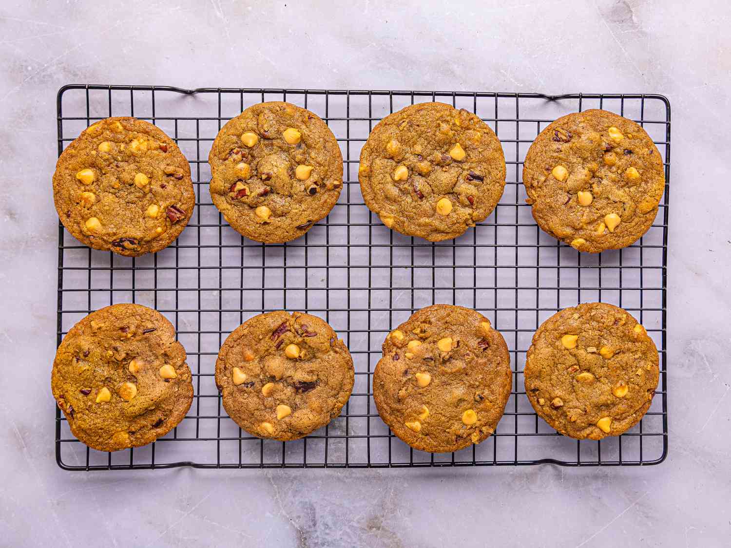 Eight cookies on a cooling rack, arranged in rows, showcasing baked texture and pieces of butterscotch and other ingredients