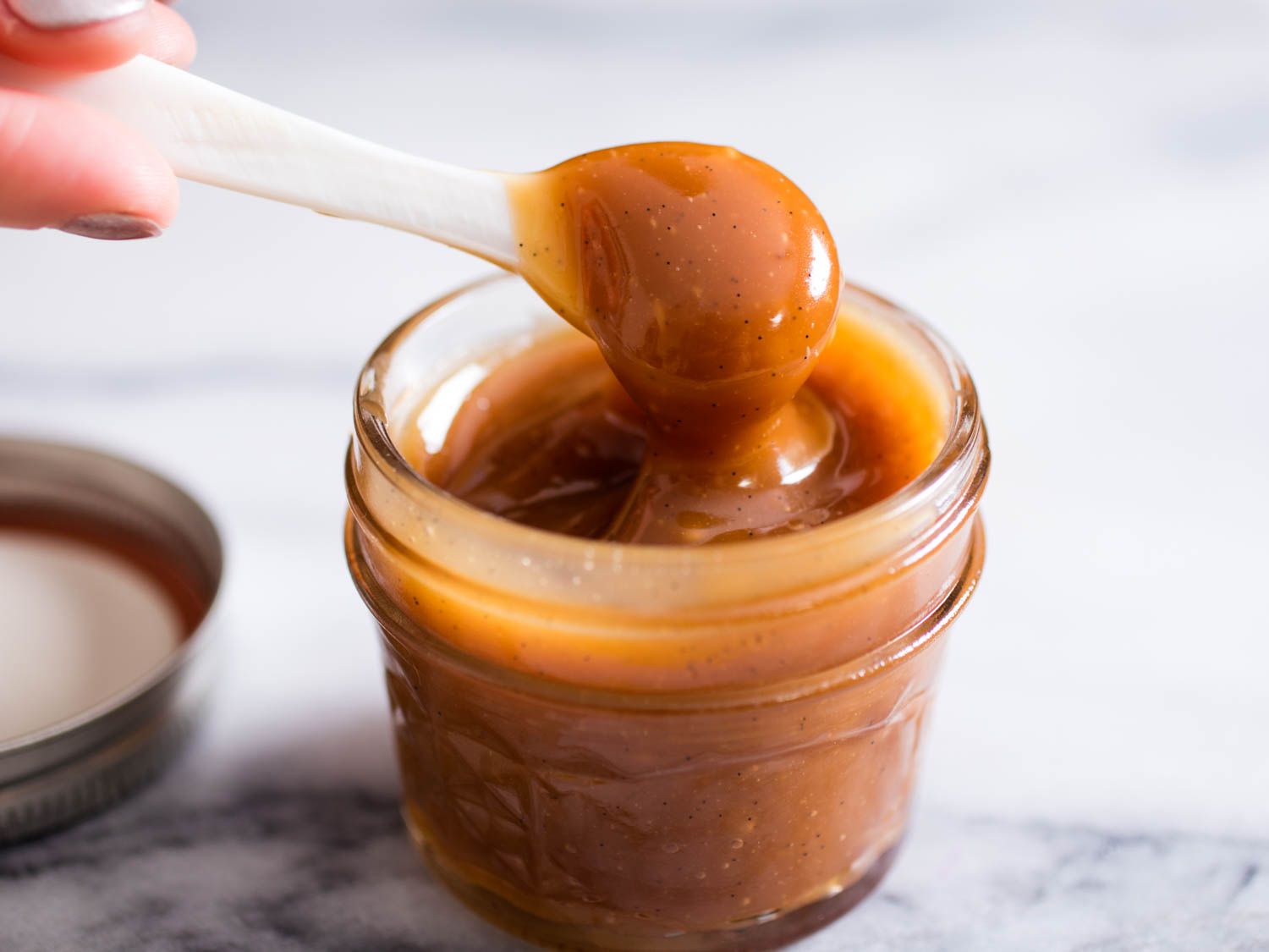 Lifting a spoonful of vanilla bean-studded caramel from a glass jar.