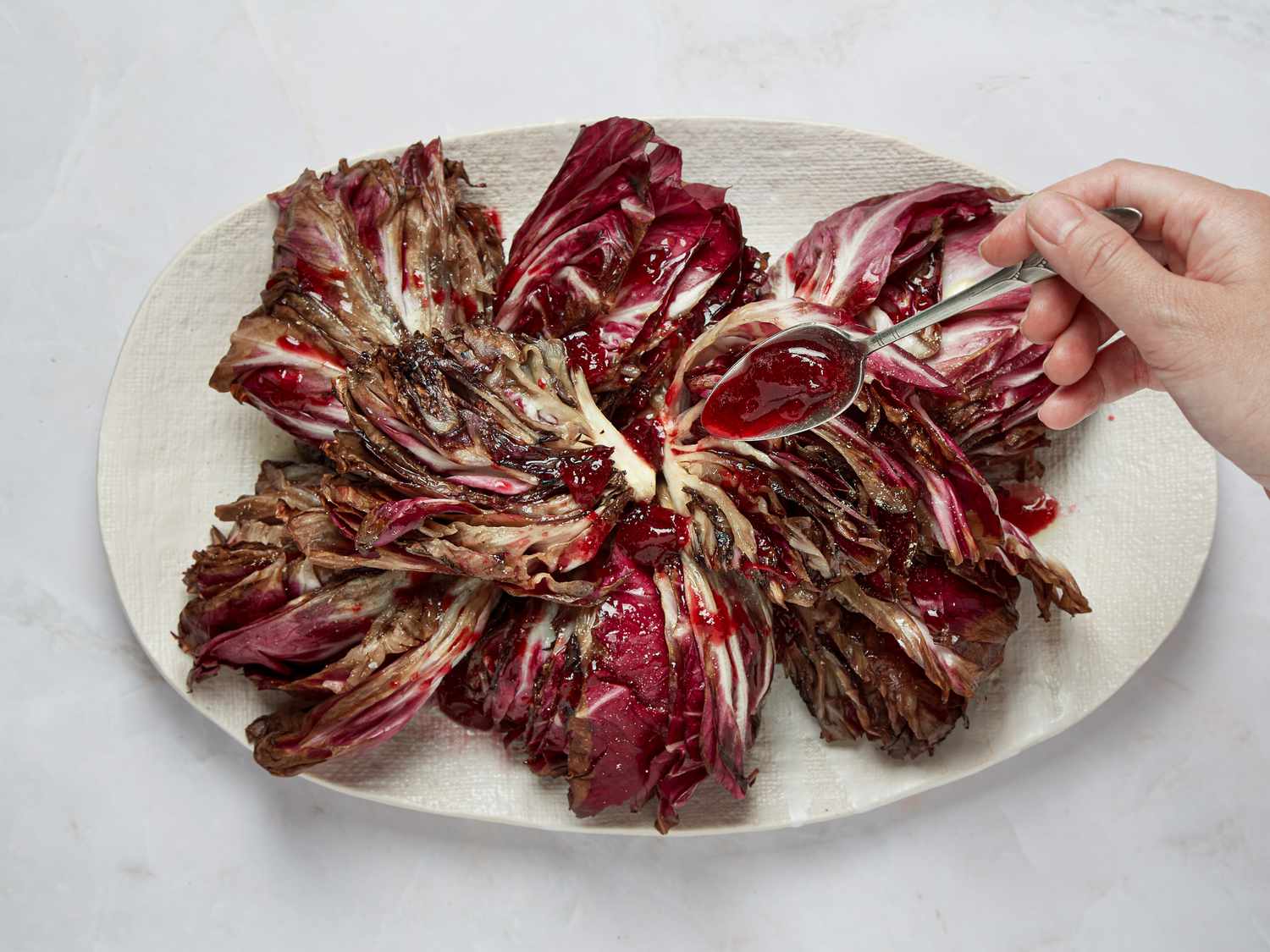 Grilled radicchio being drizzled with a sauce, served on a white plate