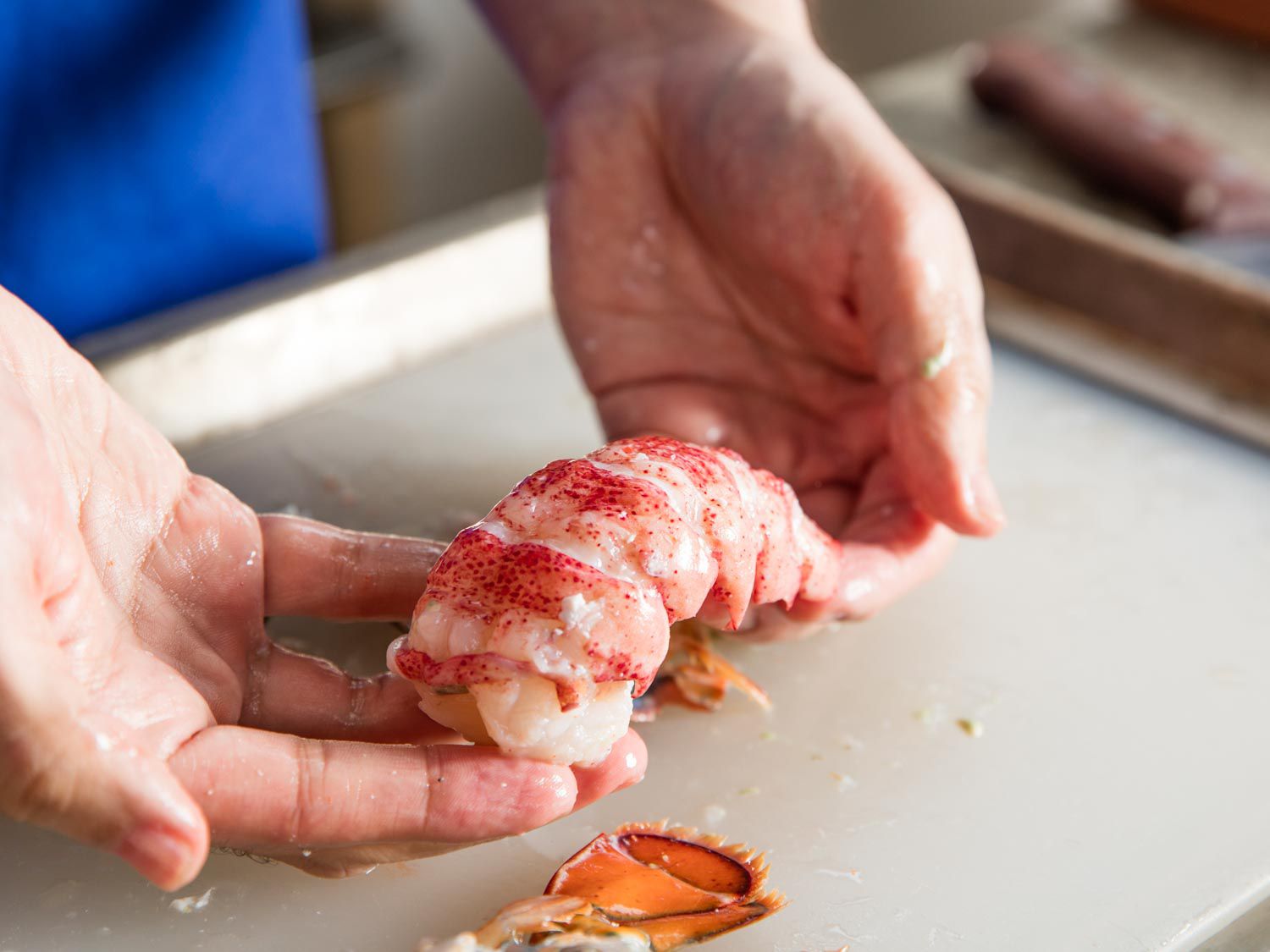 Hands cradling a perfectly shelled, intact portion of cooked lobster tail meat.