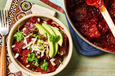 Overhead view of a bowl of chili con carne topped with avocado slices and cilantro next to the pot of chili. 