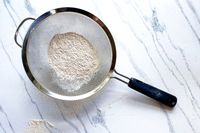 OXO Good Grips 8-Inch Double Rod Strainer with flour resting on a marble countertop