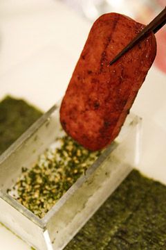 A cooked and crispy slice of spam being held by chopsticks