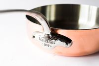 A Mauviel 1830 cookware pot with a shiny metal handle and a copper exterior
