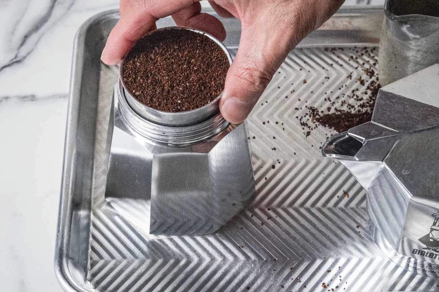 A person situating coffee grounds inside the Bialetti Moka Express moka pot.