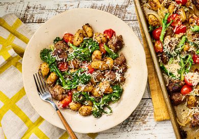 A plate of gnocchi with roasted vegetables and cheese, next to a sheet pan with more of the dish
