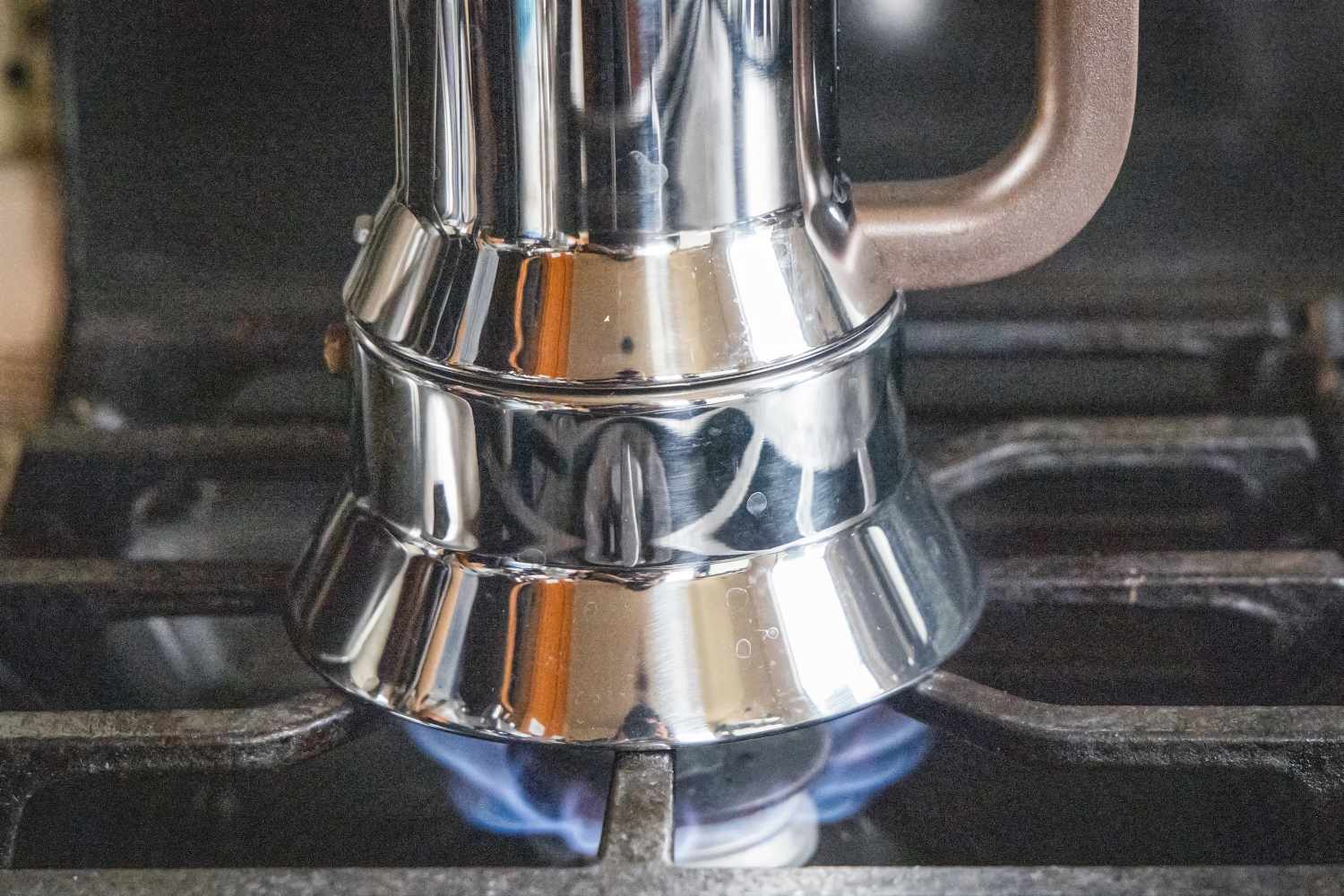 A moka pot coffee maker brewing on a gas stove