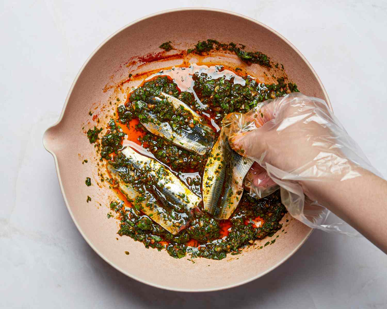 A hand prepares sardines marinaded in chermoula sauce in a dish