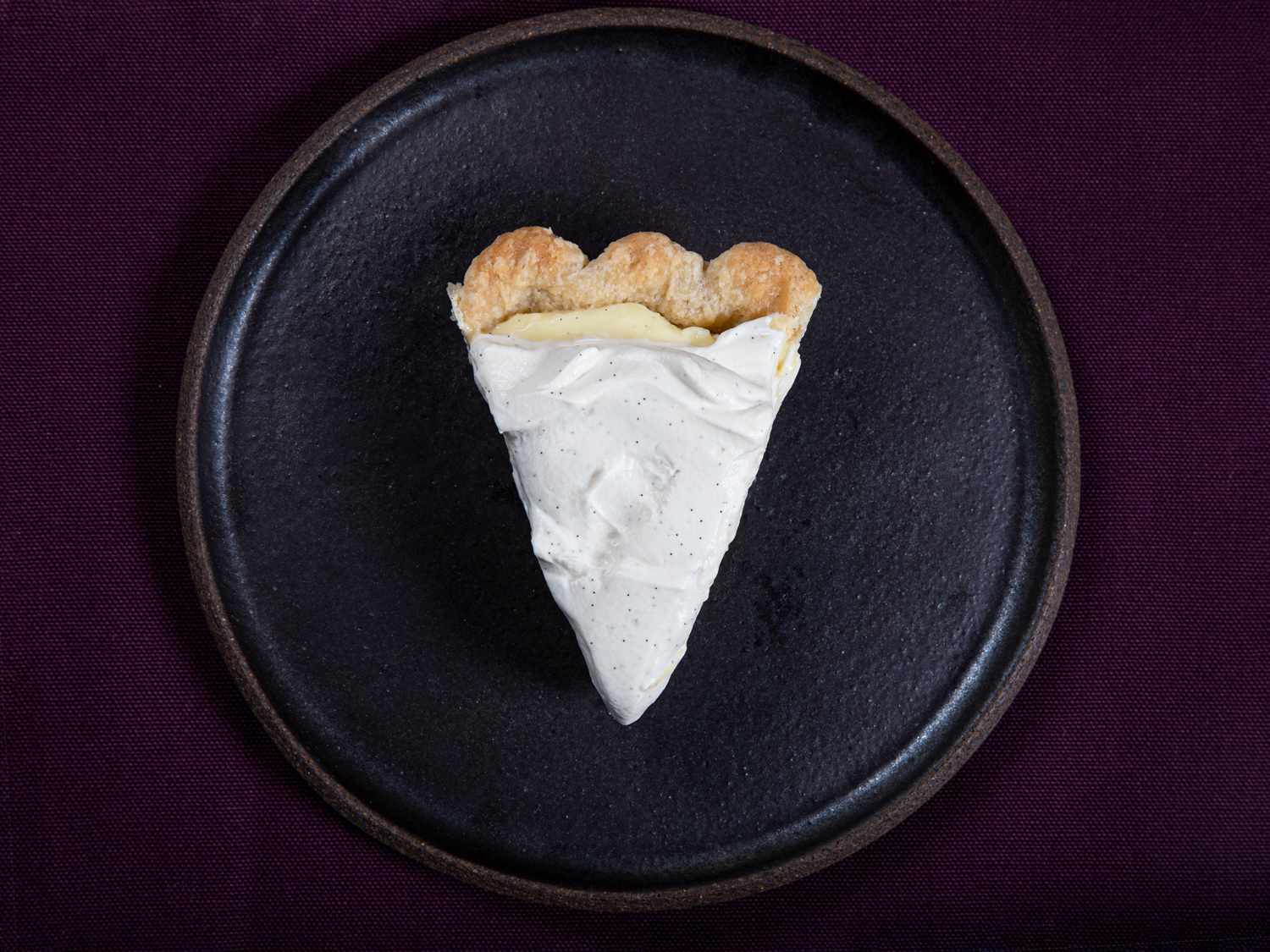 A single slice of banana cream pie on a dark plate on a purple background