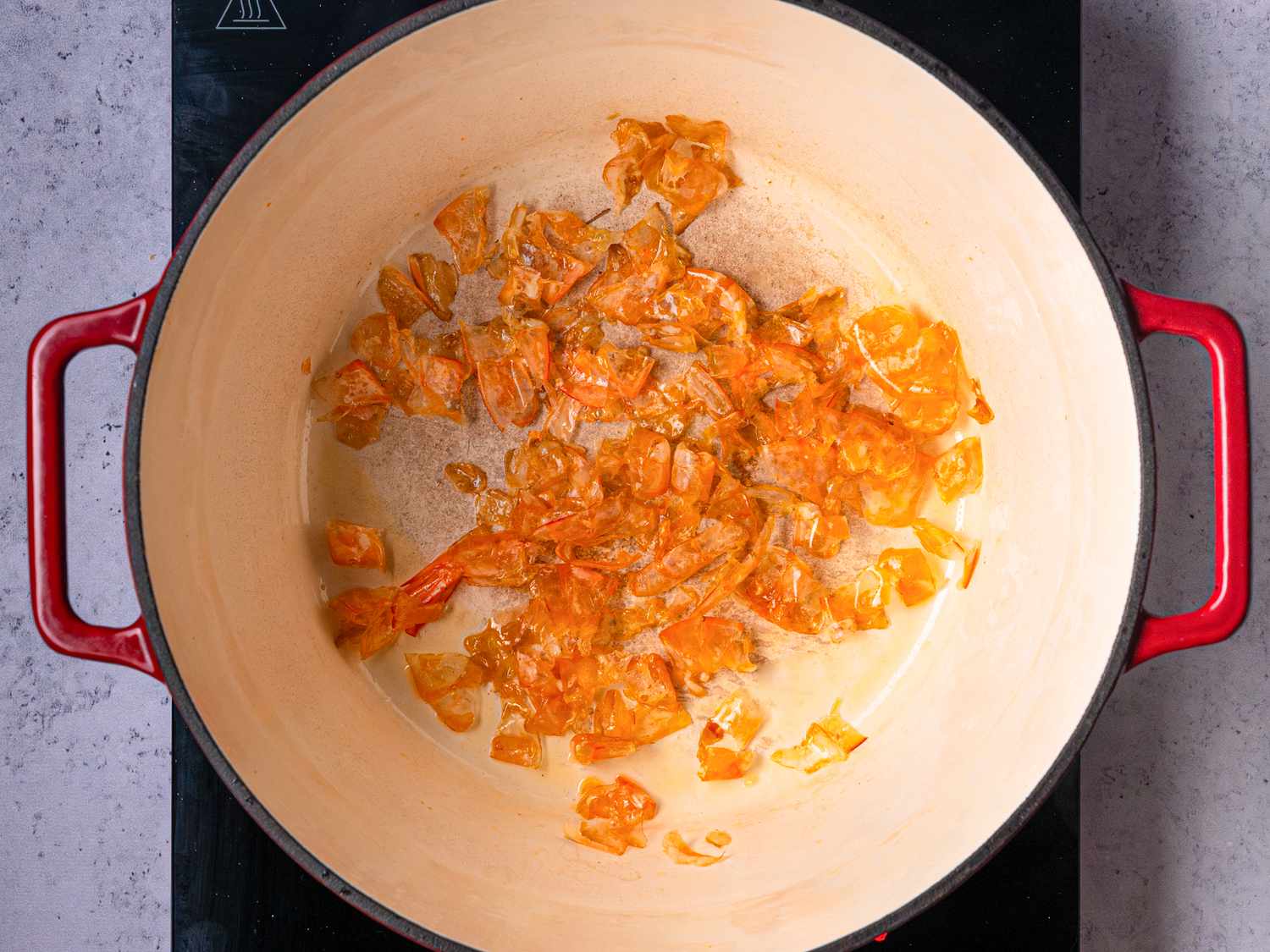 A redhandled pot with sauted ingredients on a stovetop