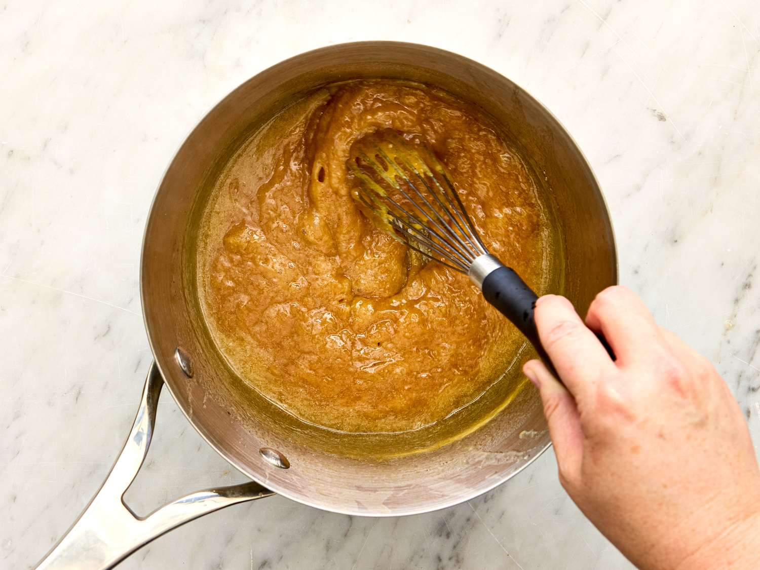 Hand whisking a mixture in a saucepan on a marble surface