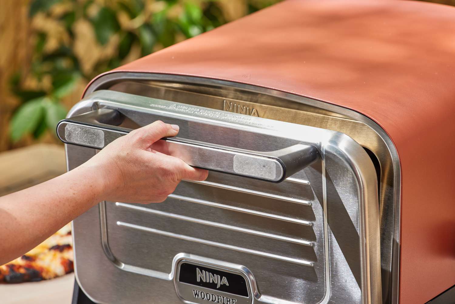 A hand holding a handle on the Ninja Woodfire 8-in-1 Outdoor Oven