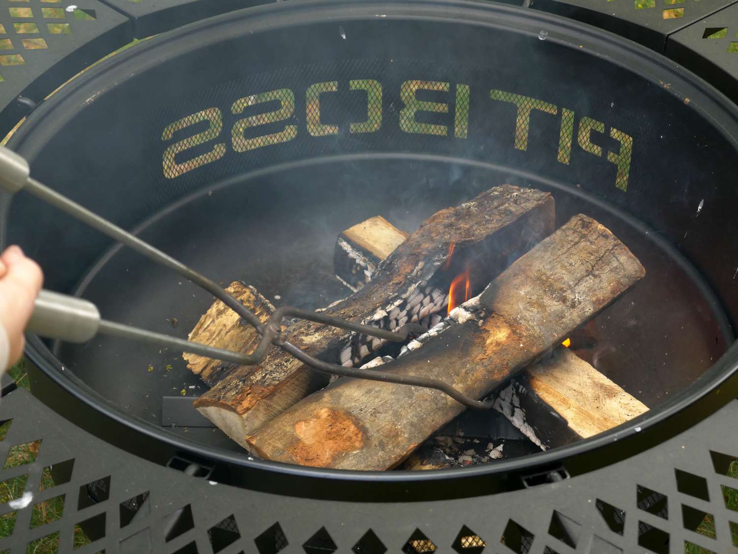 A person using fire pit tongs to adjust a log in a fire pit