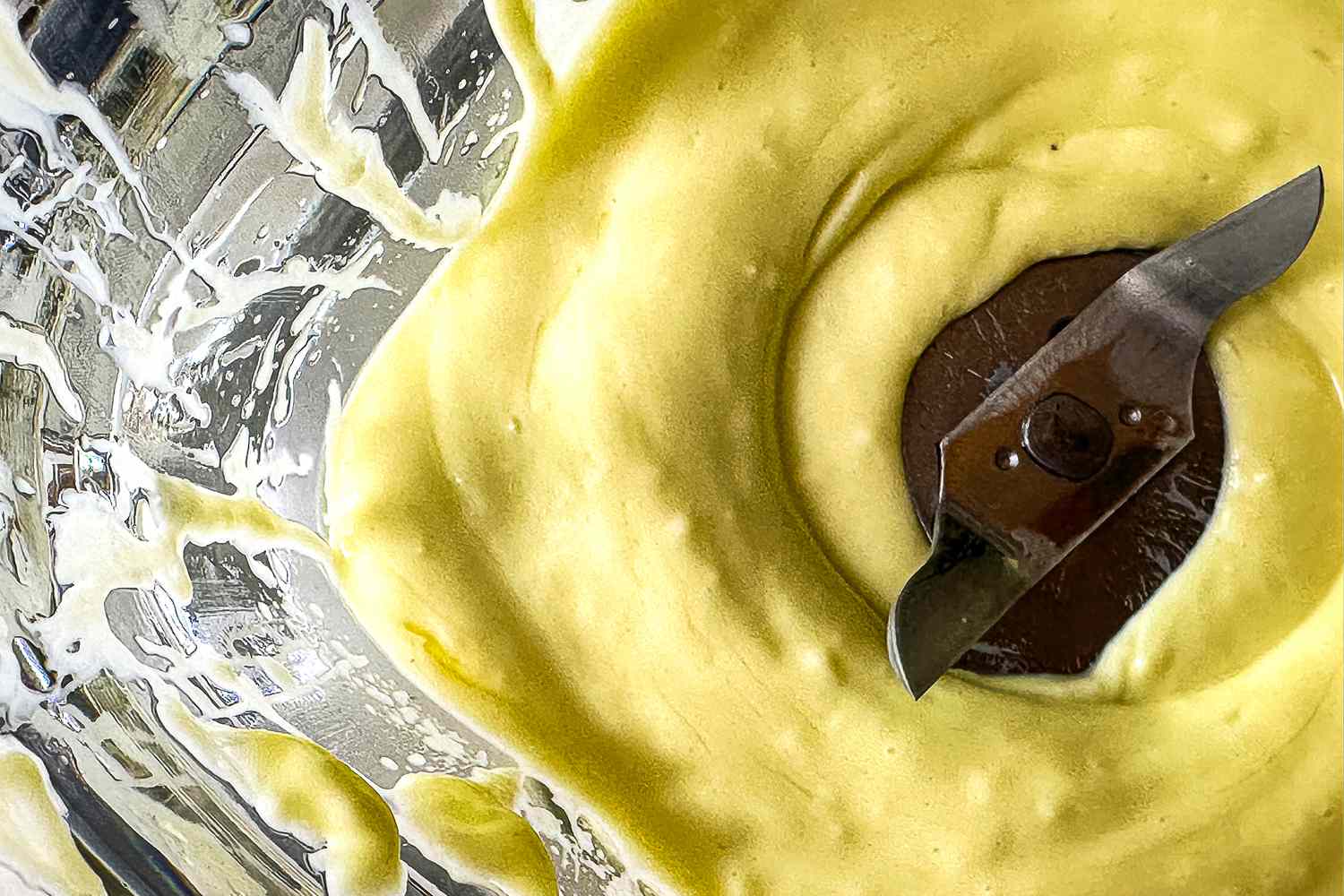 A closeup overhead view into a blender with fresh mayonnaise around the blades