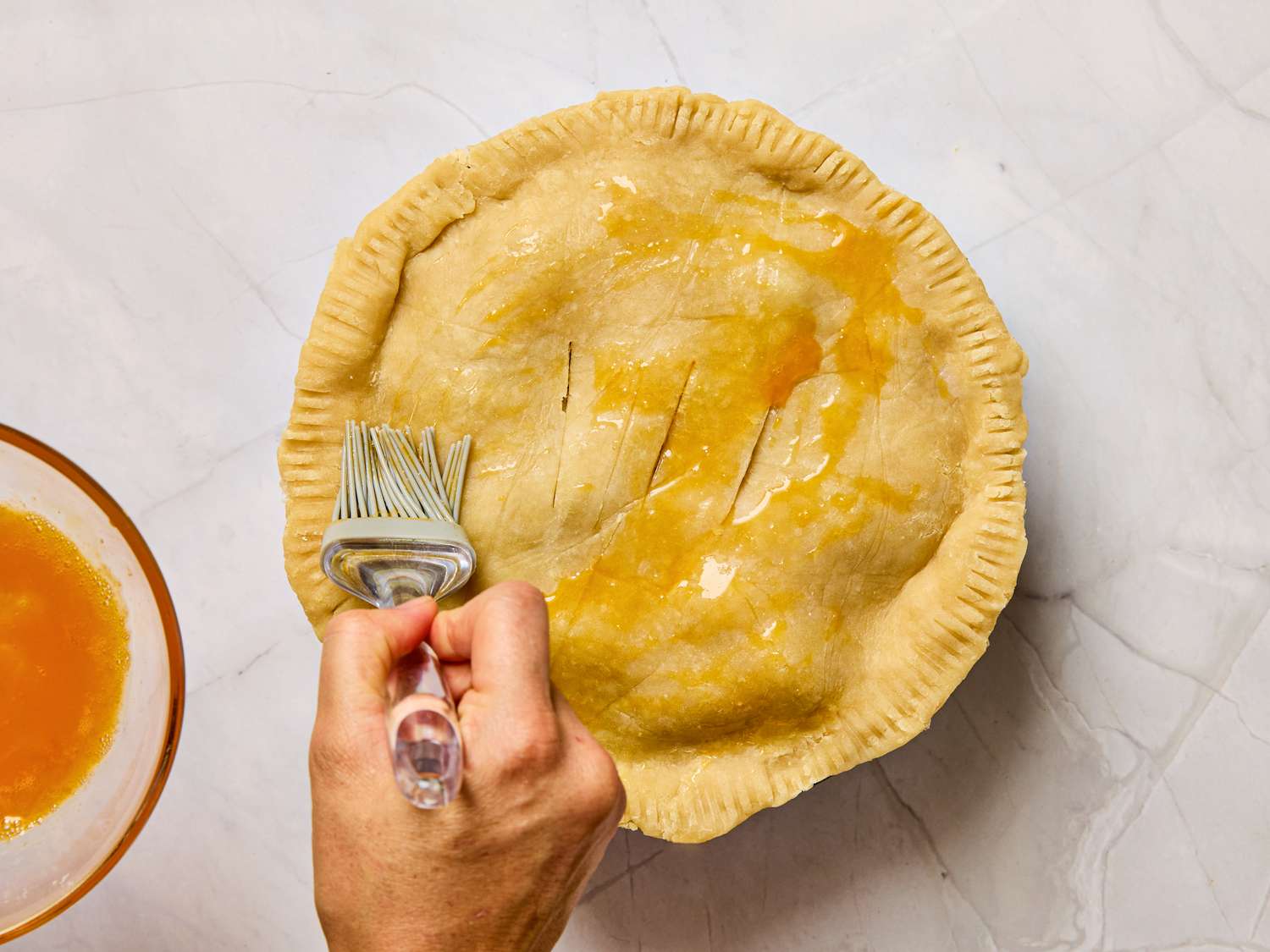 A person brushing egg wash onto pie crust before baking