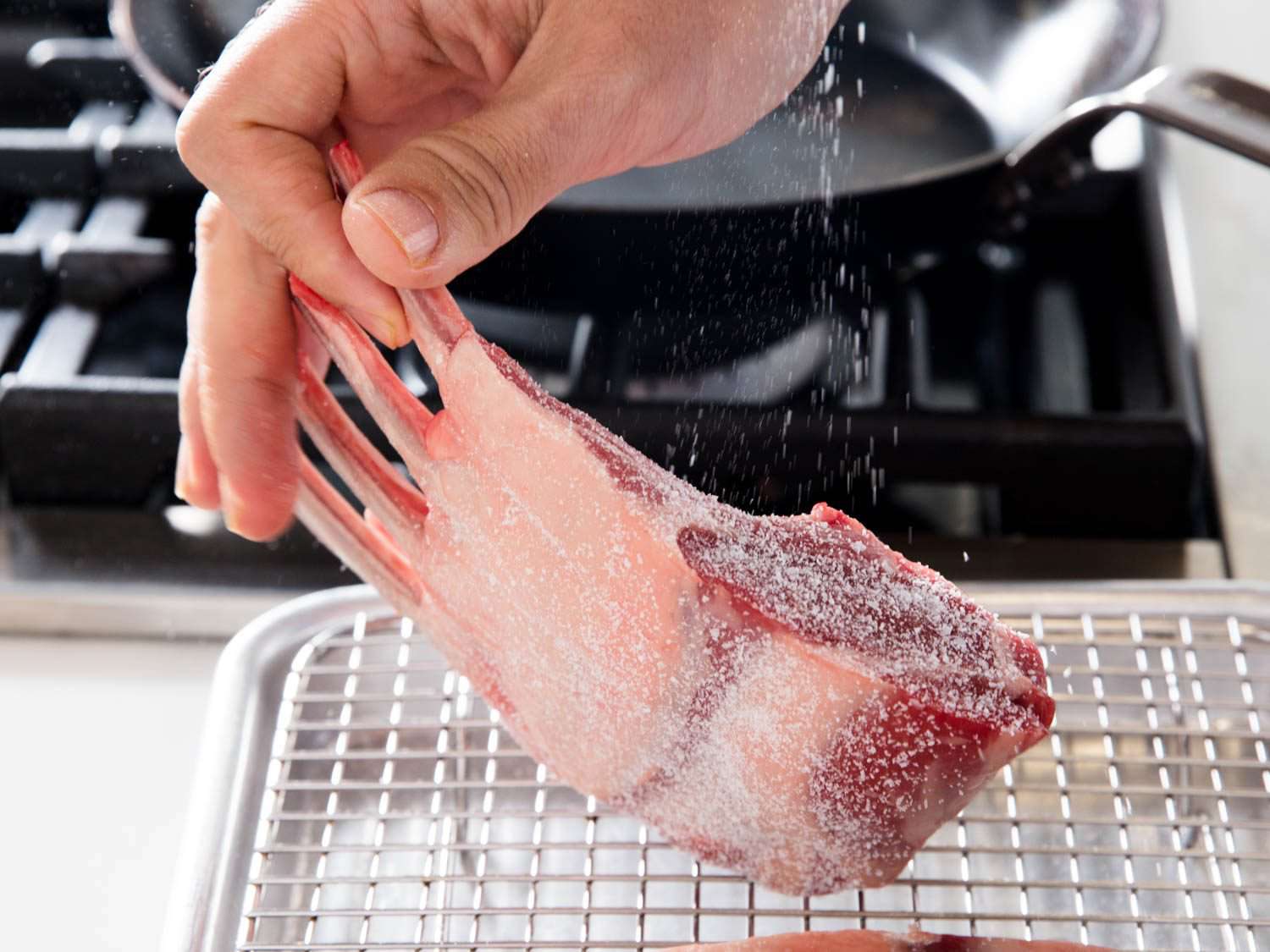Seasoning a rack of lamb all over with salt