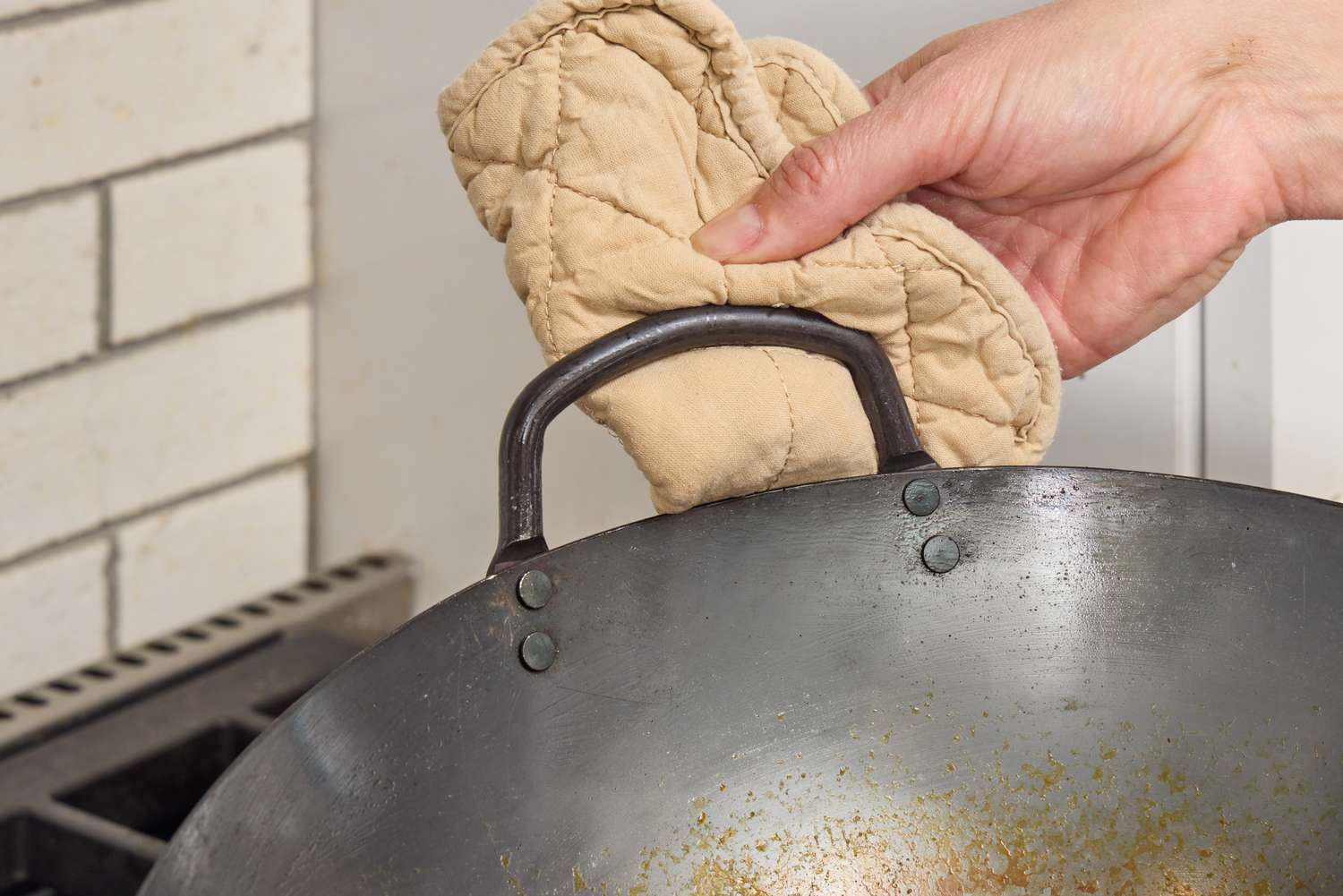 A person holds the Mammafong Pre-Seasoned Blue Carbon Steel Flat-Bottom Pow Wok by the side handle