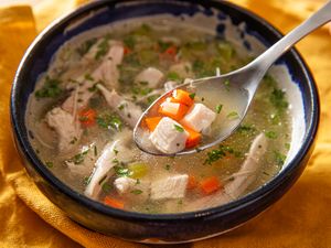 A bowl of chicken soup with a spoon holding a bite of meat and vegetables